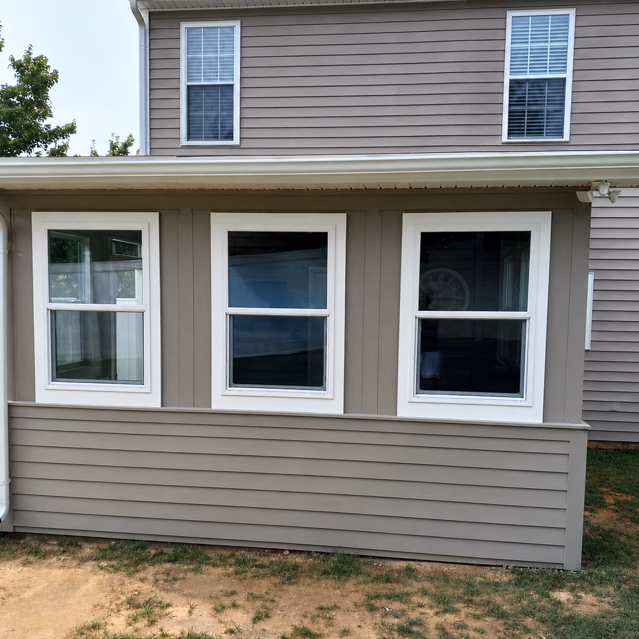 House exterior with three double-hung white-framed windows and beige siding on a grassy yard.