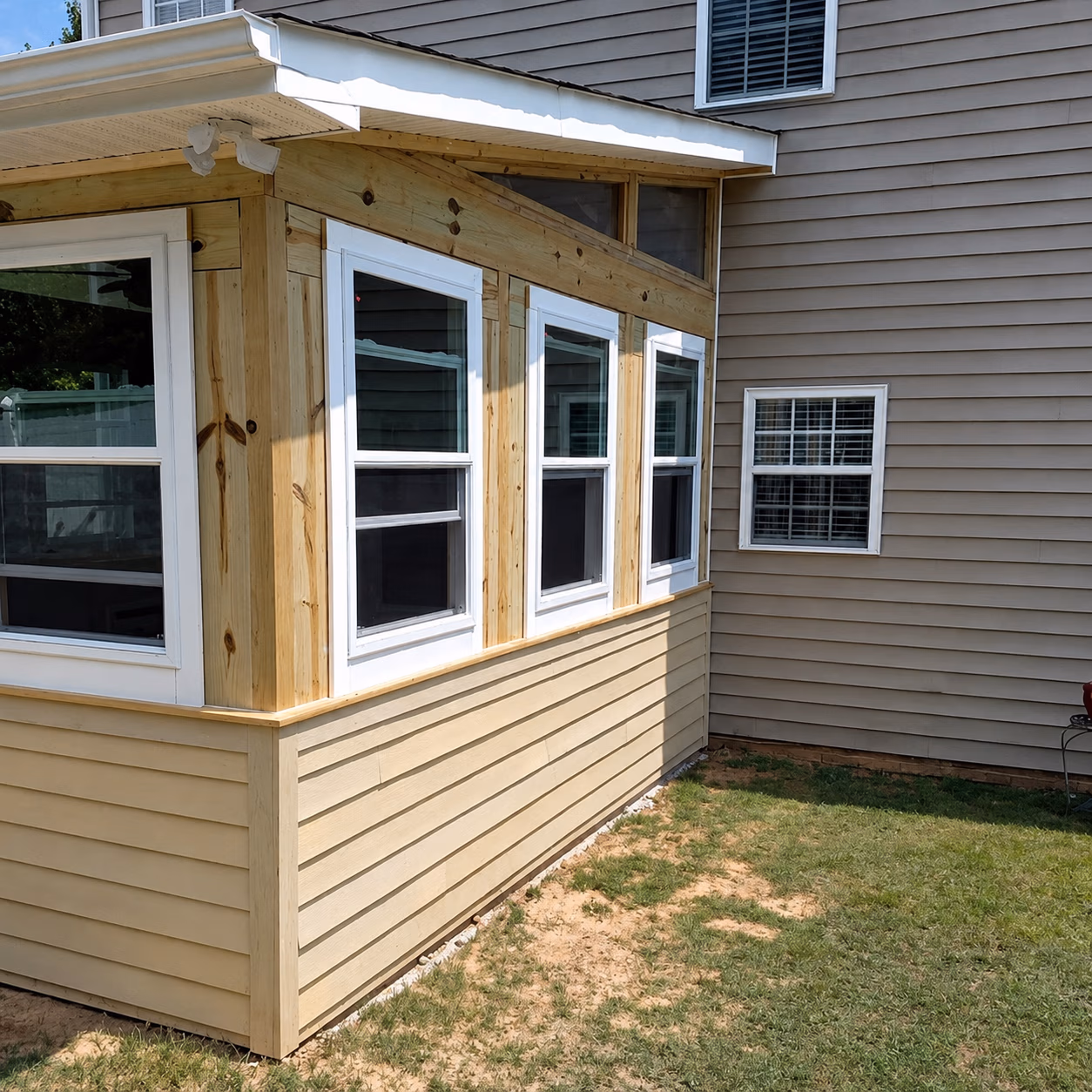New wooden and beige siding addition with multiple white-framed windows on a house.
