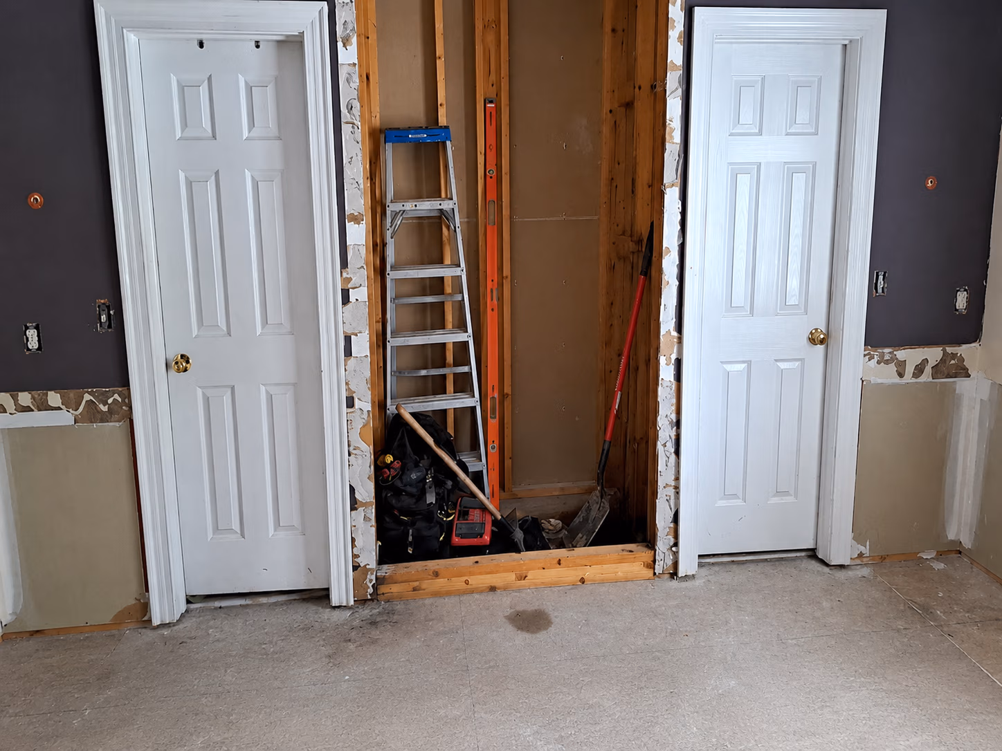 Room under renovation with two white doors and an open space filled with tools and a ladder.