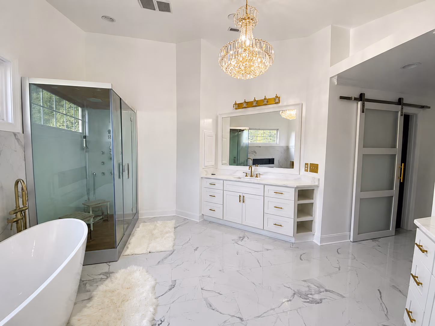 Modern bathroom with white marble floor, freestanding tub, glass shower, vanity, and chandelier.