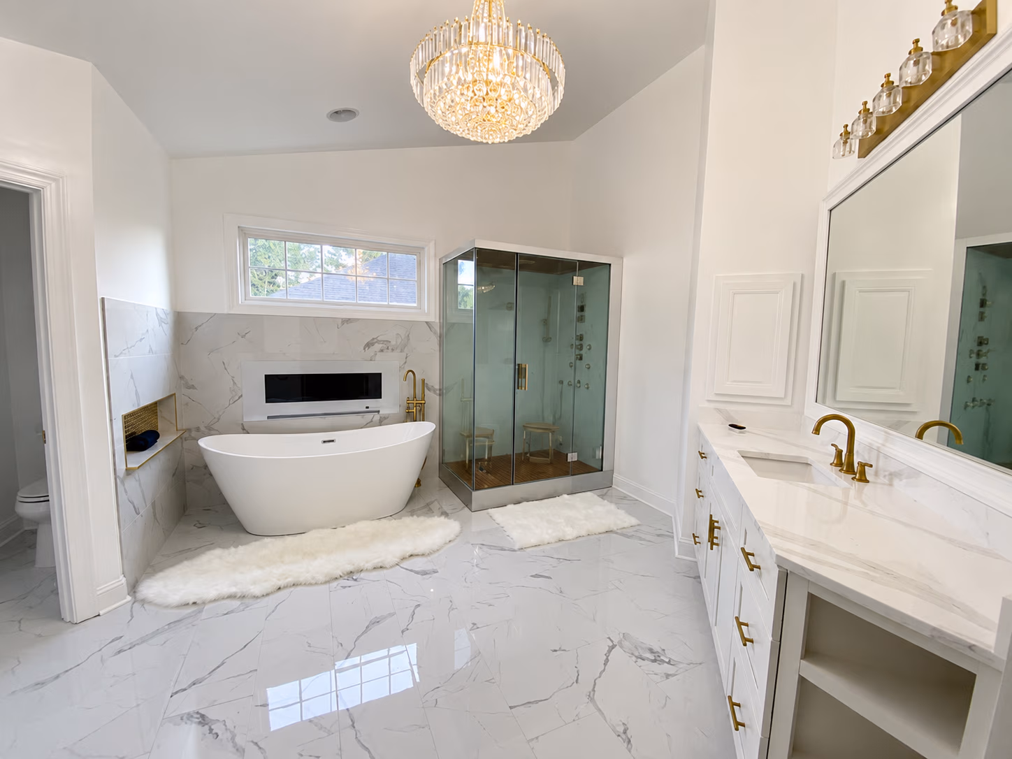 Modern bathroom with freestanding tub, glass shower, large mirror, and gold fixtures in marble decor.