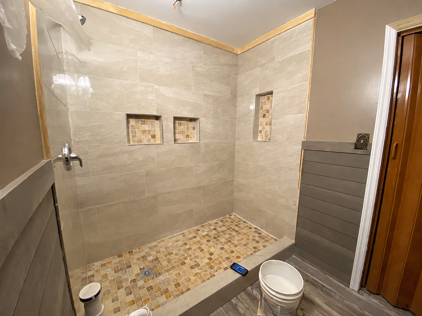 Newly tiled walk-in shower with beige wall tiles, mosaic floor, and three built-in wall niches.