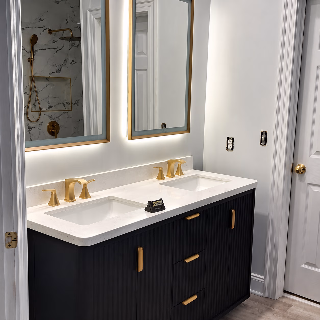 Modern bathroom vanity with dual sinks, gold fixtures, black cabinet, and two mirrors with backlighting.