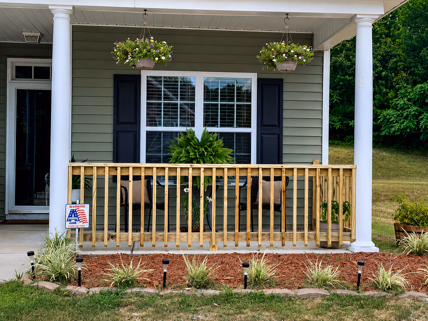 House porch with wooden railing, two hanging flower baskets, a window, and outdoor chairs.