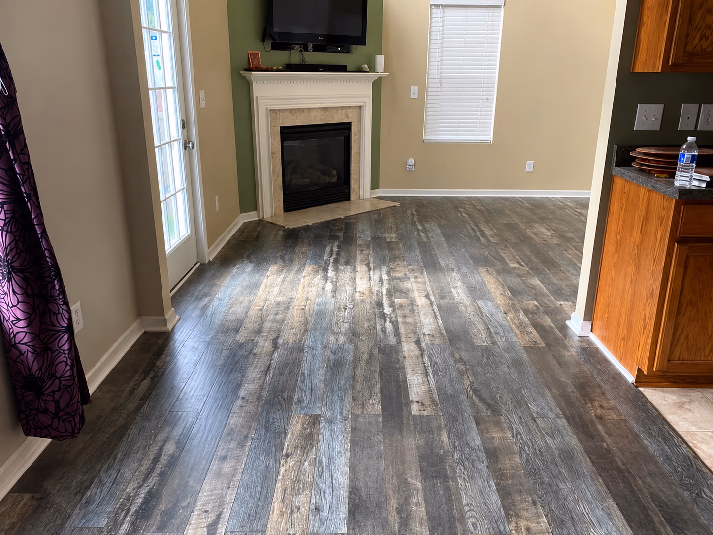 Empty living room with dark wood laminate flooring, fireplace, TV on wall, and kitchen cabinetry.