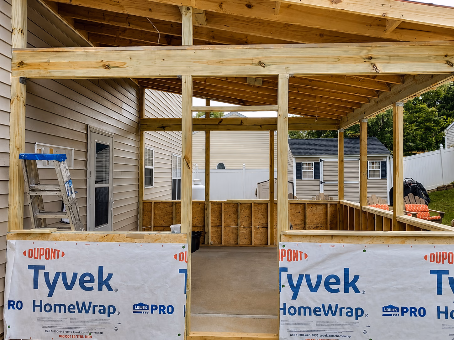 Wooden framing structure for a home addition with Tyvek HomeWrap on lower walls and a ladder on the side.