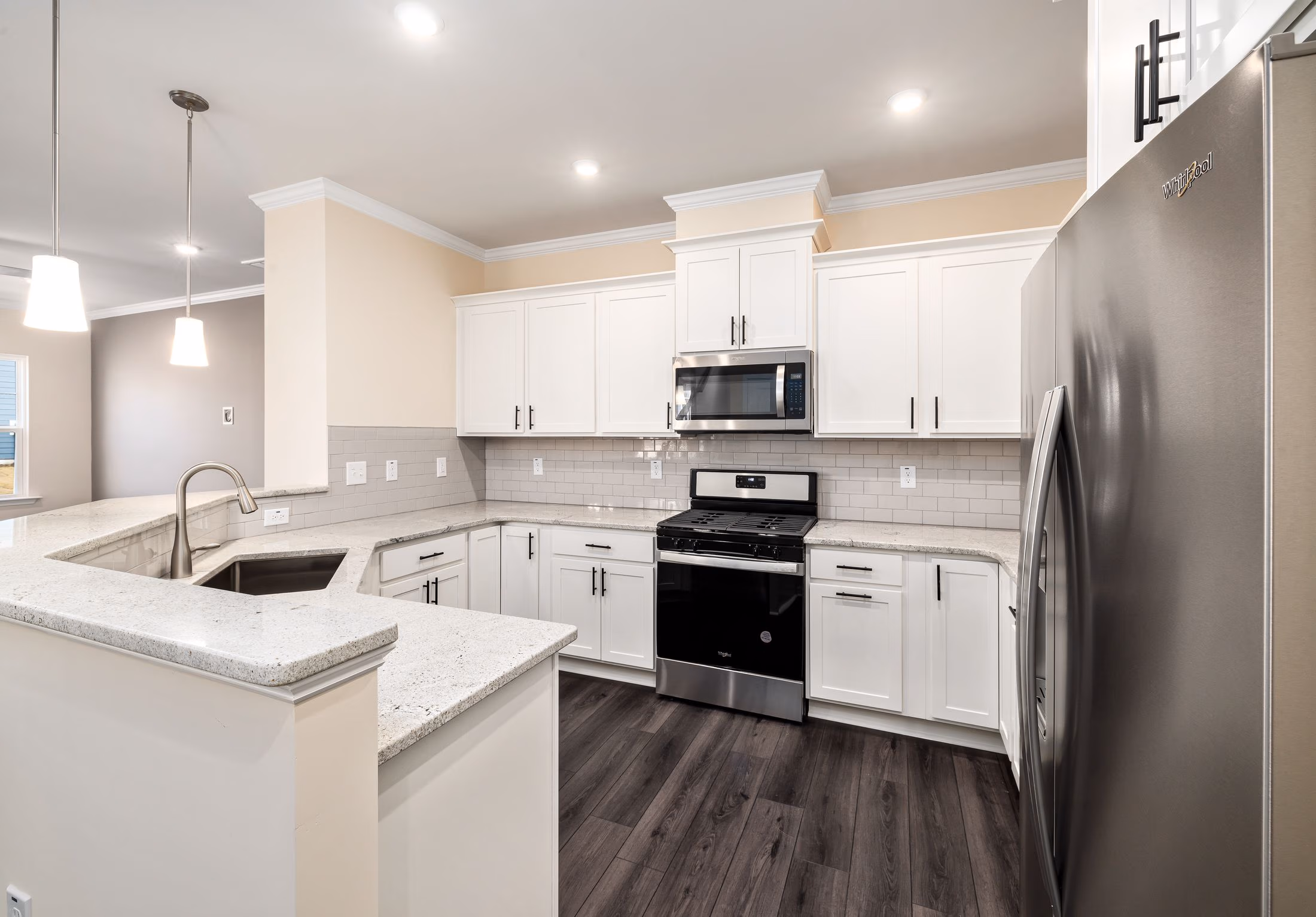 Modern kitchen with white cabinets, granite countertops, stainless steel stove, microwave, and refrigerator.