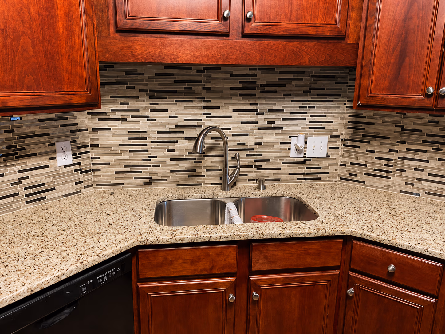 Corner kitchen sink with stainless steel double basin, granite countertop, and wooden cabinets.