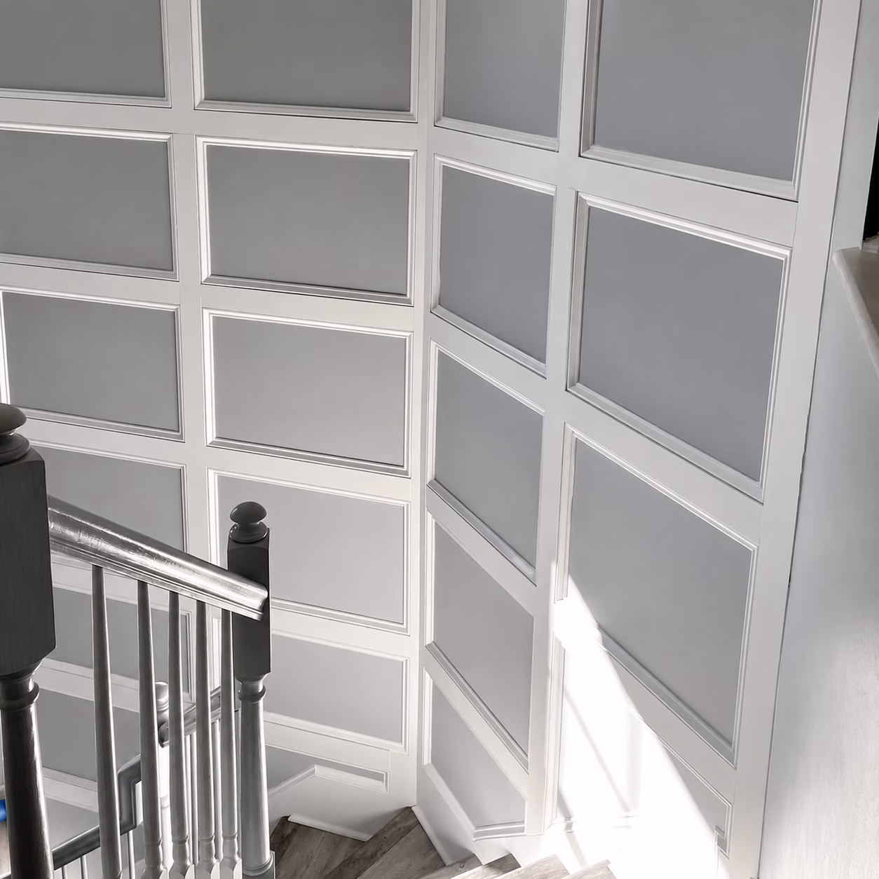 White paneled walls and a wooden staircase with white balusters in natural light.