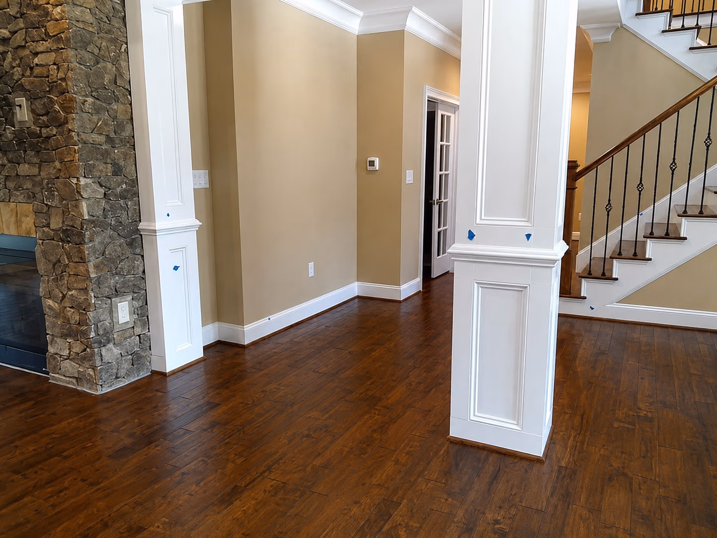 Interior room with wood floors, beige walls, white pillars, stone fireplace, and staircase with wood railing.