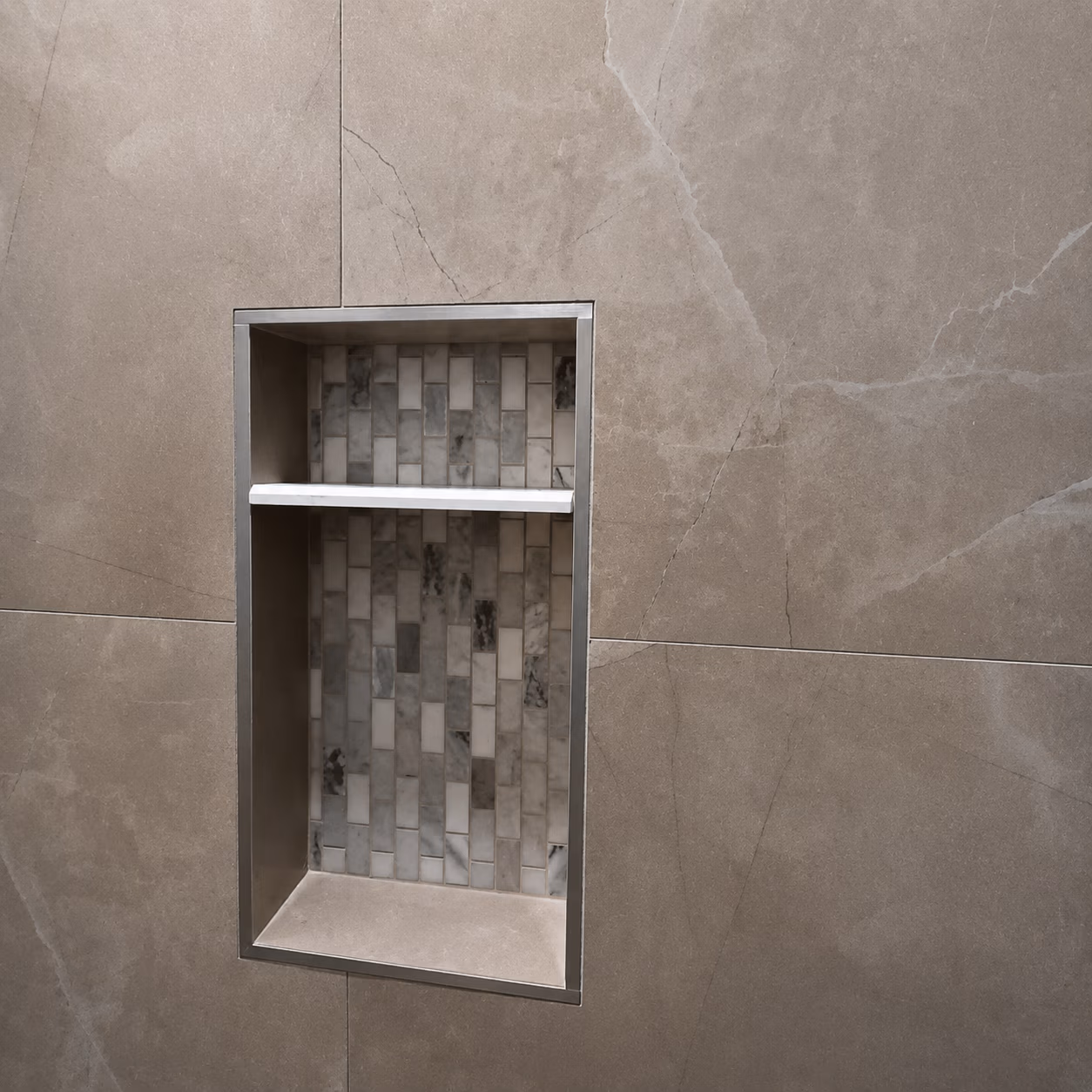 Built-in shower niche with mosaic tile back and a white corner shelf on beige tiled wall.