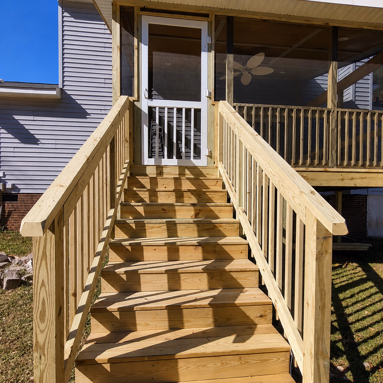 Wooden outdoor stairs with railings leading to a screened porch and white door.