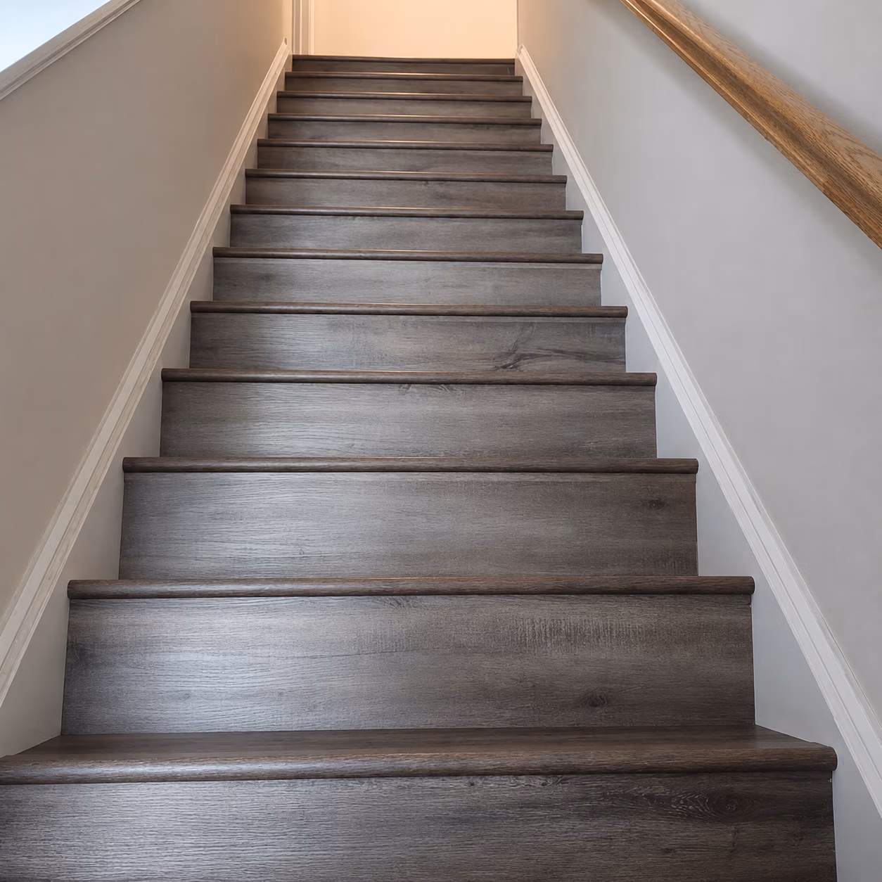 Dark wooden stairs with white walls and a wooden handrail on the right side.