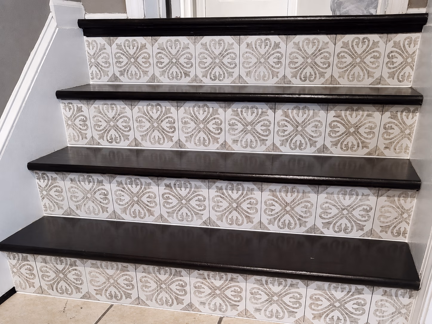 Four black wooden stairs with white and gray decorative patterned tile risers.
